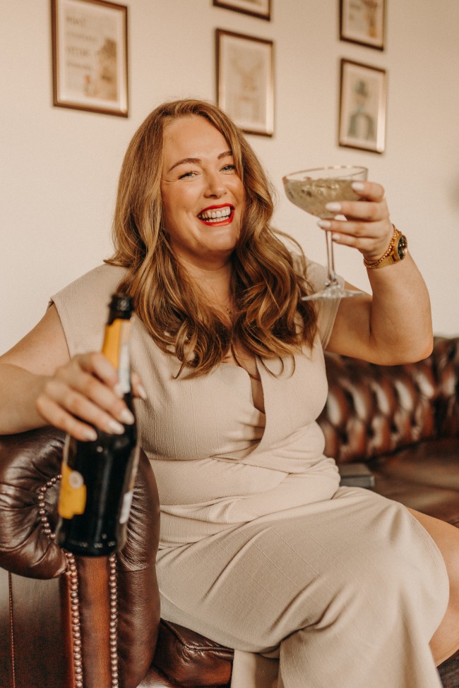 Digital Marketing Consultant & SEO Specialist Aoibhinn Cullen from The OG Marketing Agency sits in a leather chair with champagne bottle in ione hand and a glass in the other hand